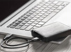 Ordinateur portable connecté à un disque dur externe via USB sur une table en bois.