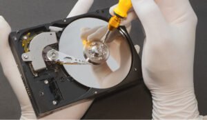Une personne en gants manipule un disque dur ouvert avec un tournevis.
