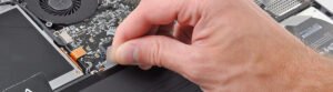 Main réparant ou maintenant un ordinateur portable, manipulant des composants près d'un ventilateur.