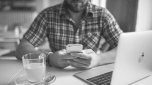 Homme avec chemise à carreaux utilisant smartphone, ordinateur portable et tasse de café.