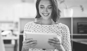 Personne souriante tenant une tablette dans un bureau, vêtue d'un haut à pois.