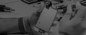 Personne en gants réparant un smartphone avec un outil sur une table de travail.