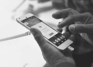 Personne utilisant un smartphone exposé, connecté par un cordon, en noir et blanc.