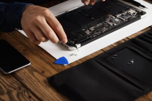 Ordinateur portable en réparation sur table en bois avec outils et smartphone.