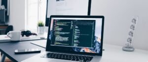 Ordinateur portable avec code, tasse, smartphone, écouteurs et écran en arrière-plan sur un bureau.